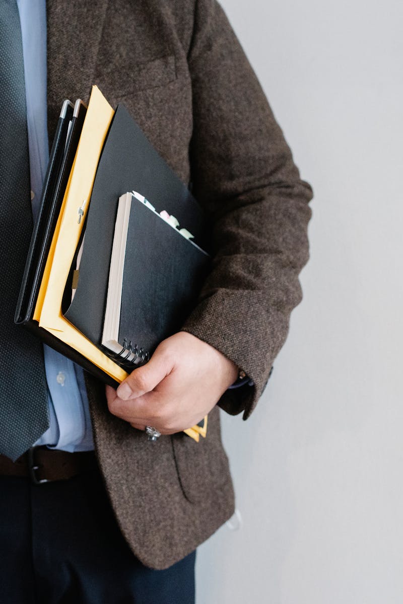 Business professional in a suit holding various folders and notebooks indoors.